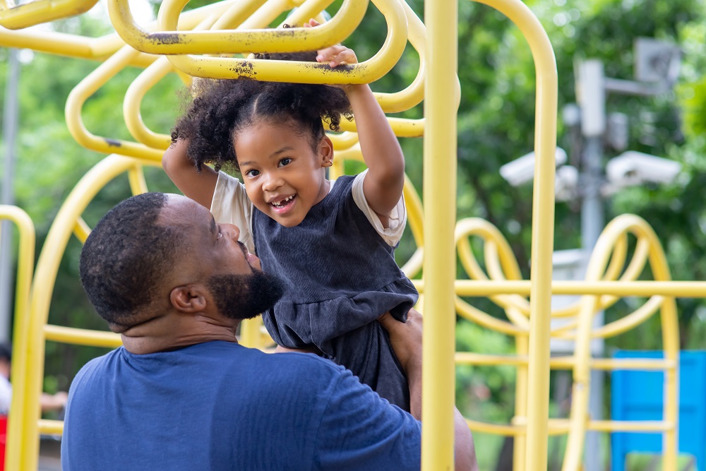 Happy Black parent carrying child playing at playground in the park.