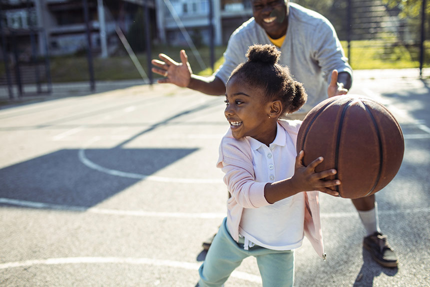 Little girl playing basketball with adult male