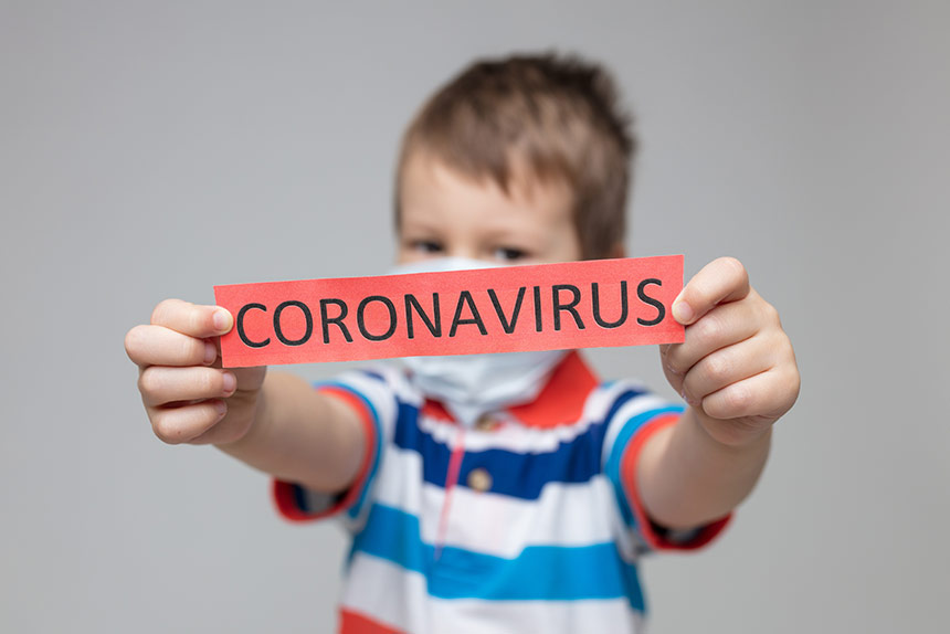 Photo of little boy holding up red piece of paper that says coronavirus
