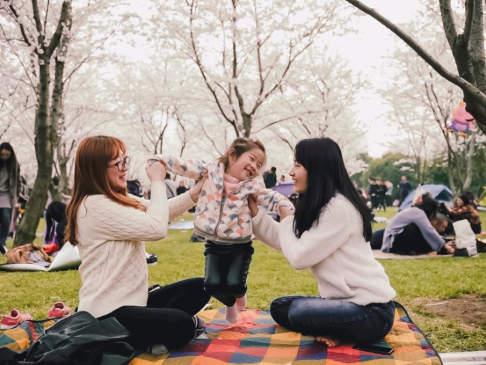 two adults and child sitting on blanket outside