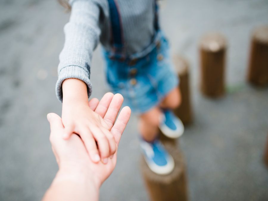 Child climbing on logs with help of parents hand.