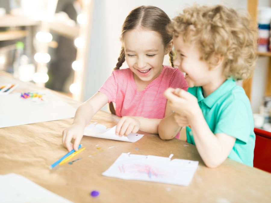 Young girl and boy coloring and laughing together.