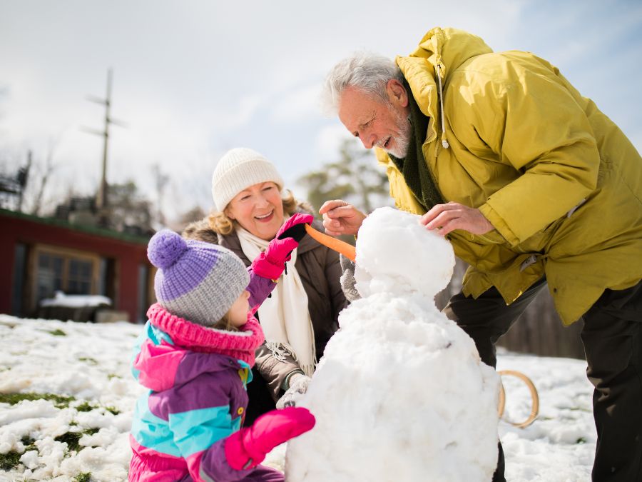 Child and grandparents building a snowman.