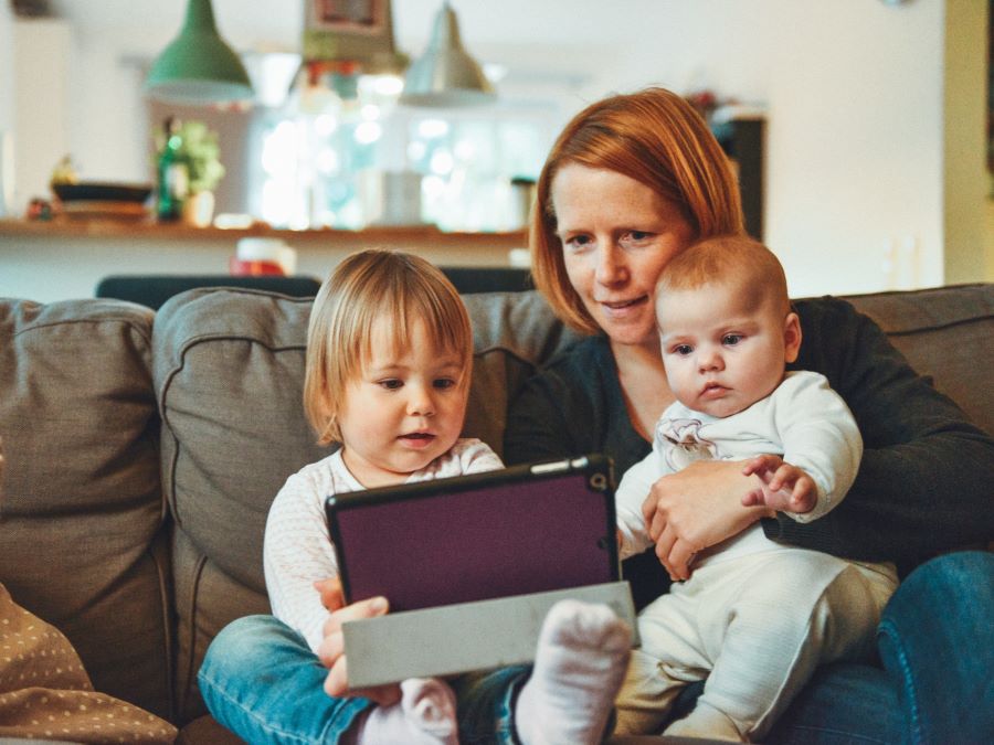 Woman and two babies watching a tablet on a sofa.