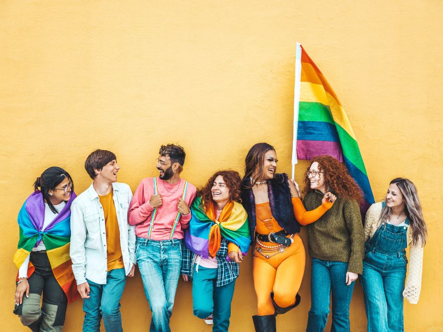 Group of friends against and orange wall holding and wearing Pride flags.