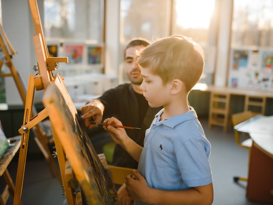 Young kid in front of easel with teacher helping him.