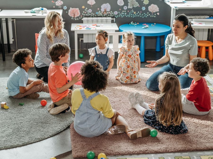 Children sitting in a circle with two teachers.