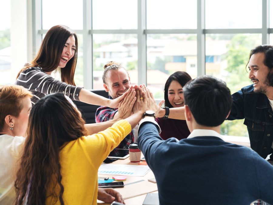 Group of adults around a desk all high fiving in the center of the table.