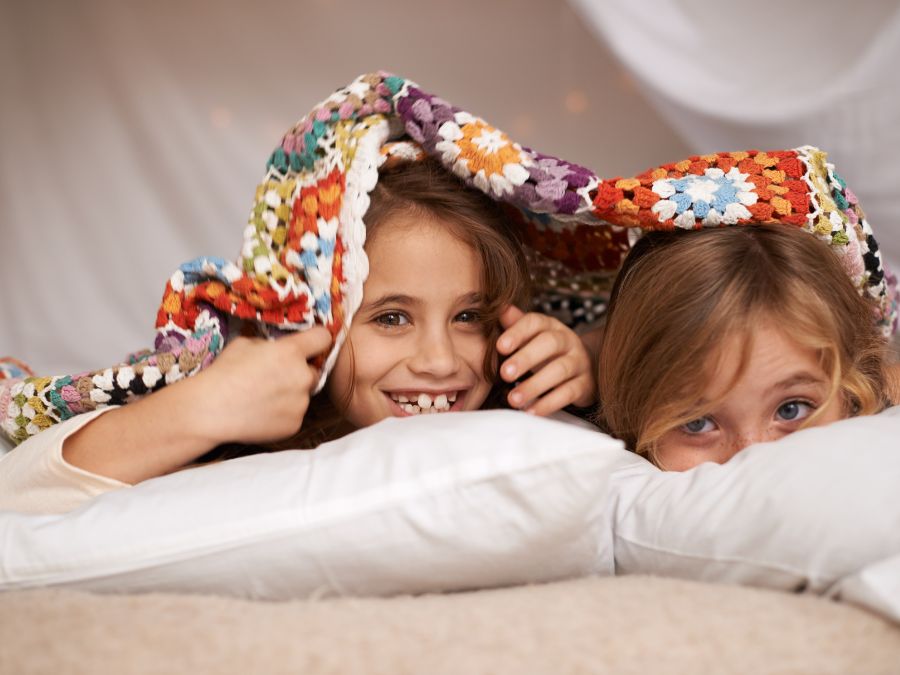 Two young kids hiding under a blanket.