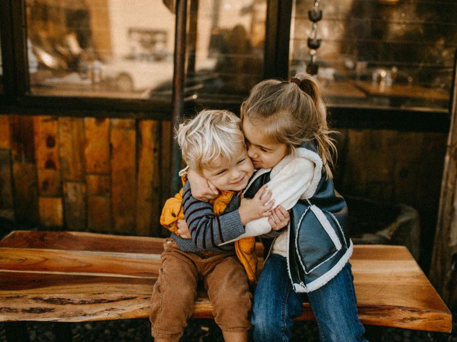 Two children sitting on a bench hugging.