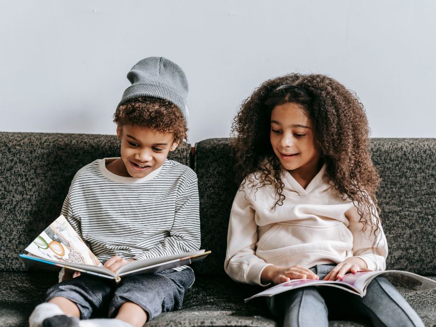 Two children sitting on a couch reading books.