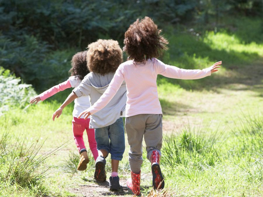 Three young kids walking down a path in the grass.