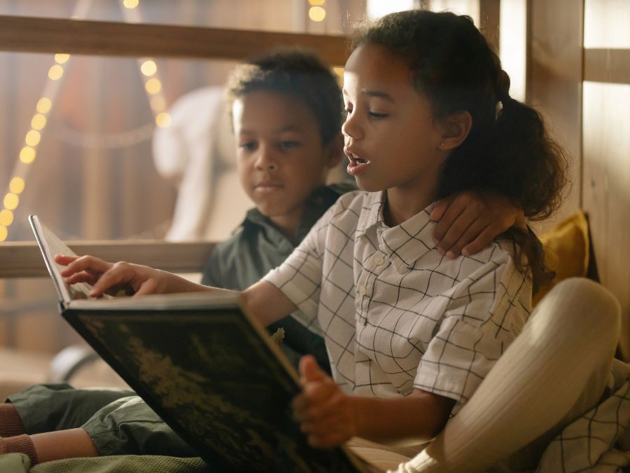 One child reading a book to a younger child.