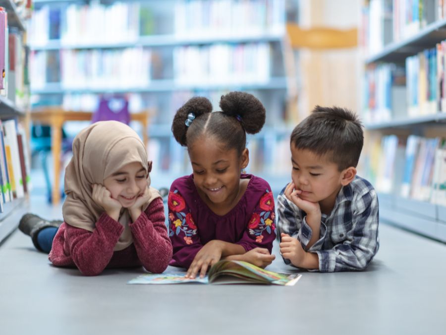 Three children reading a book at a library.