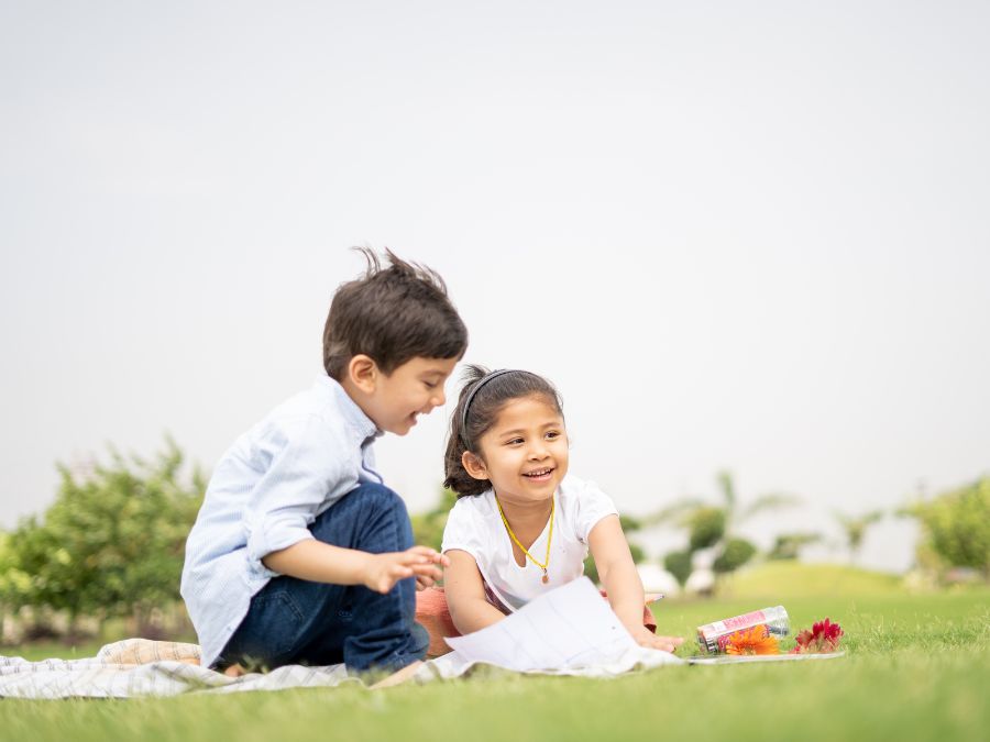 Young brother and sister sitting on a blanket in the grass.