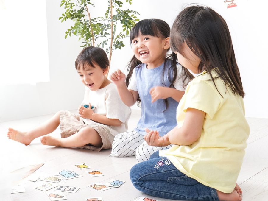 Three children playing a card game on the floor.