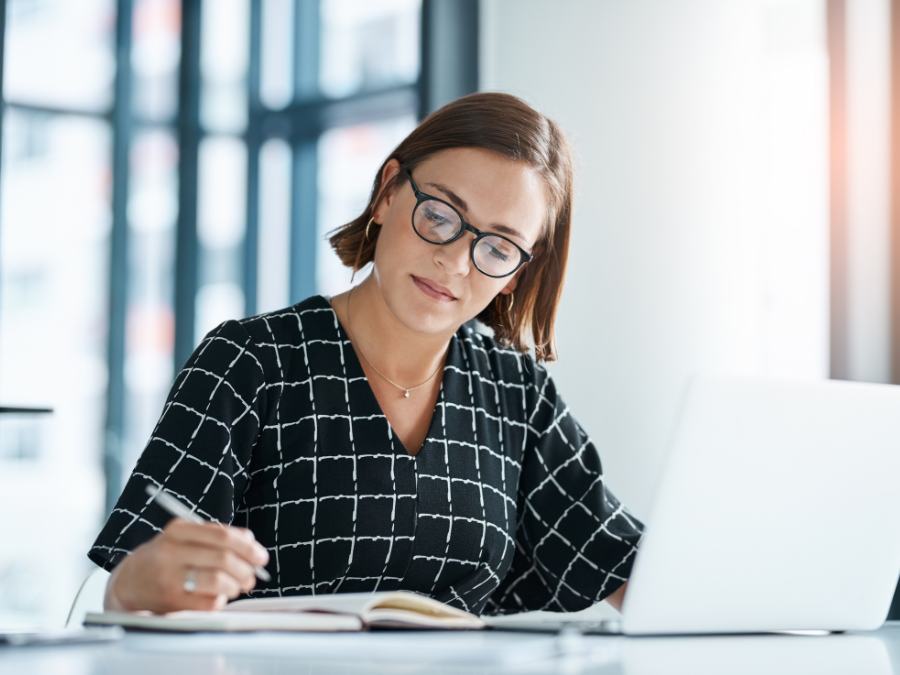 woman writing in notebook at computer