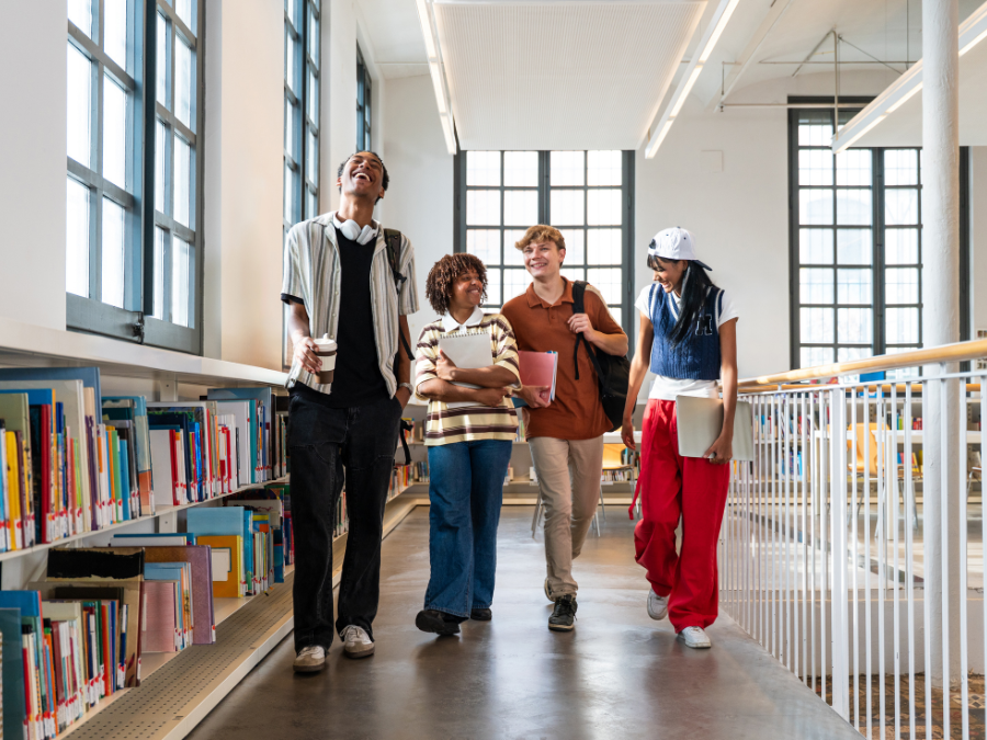 Four friends walking and laughing in a library.