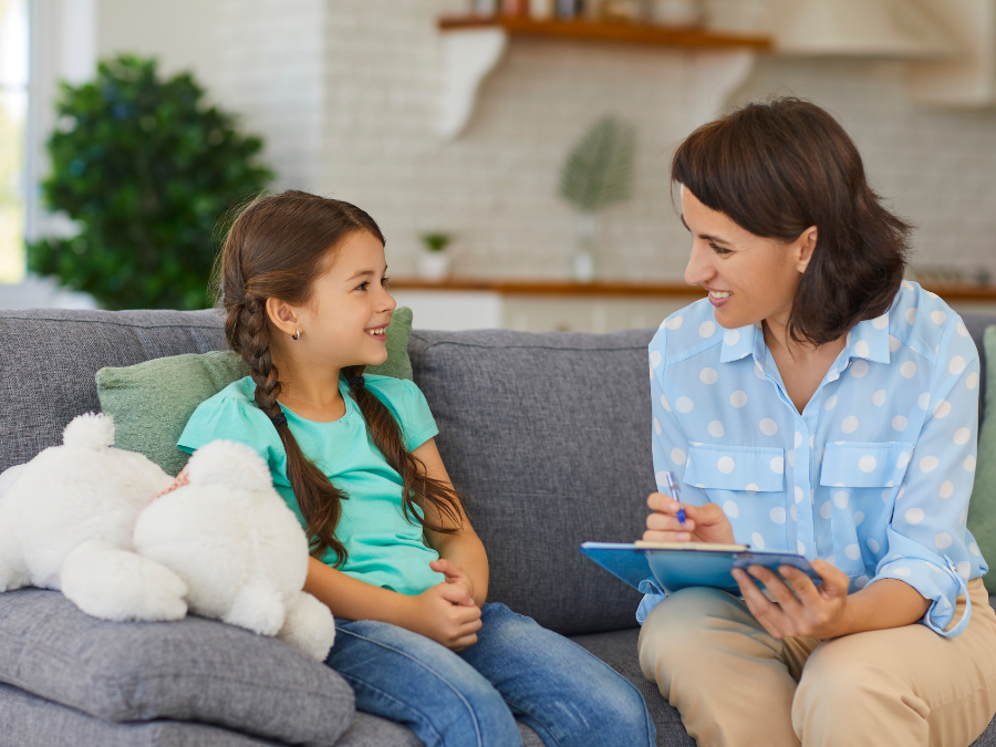 Young girl and a therapist taking notes sitting on a couch.