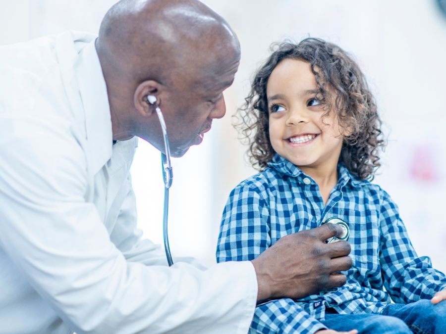 Doctor listening to child's heart. The child is smiling.